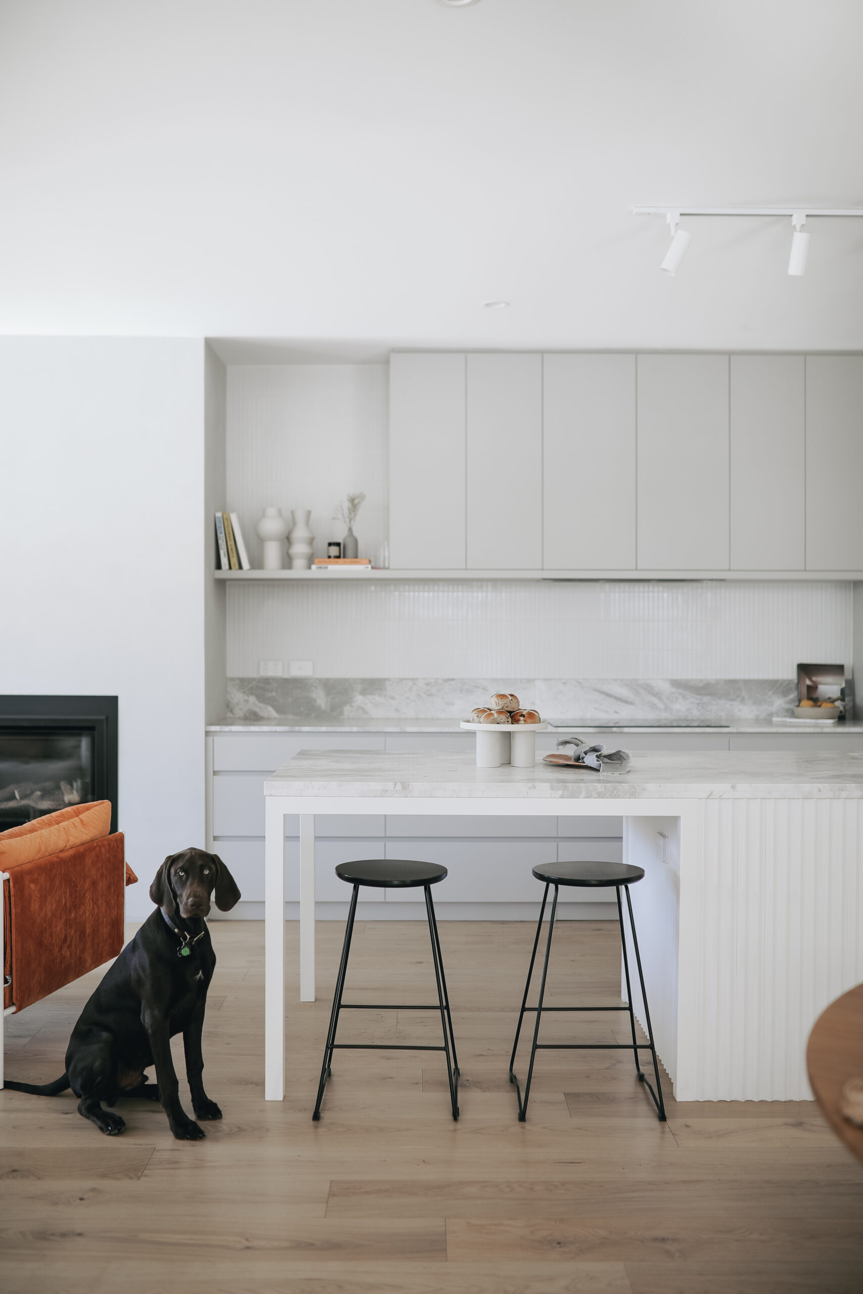 A modern kitchen with sleek white cabinetry, an island bench with dark wood paneling, stainless steel appliances, and pendant lights, showcasing the craftsmanship of expert home builders.